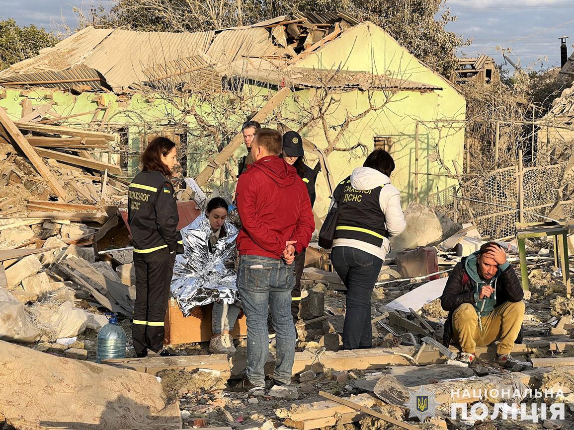 Cette photo prise et publiée par la police nationale ukrainienne le 9 octobre 2022 montre des résidents locaux assis devant les maisons endommagées.